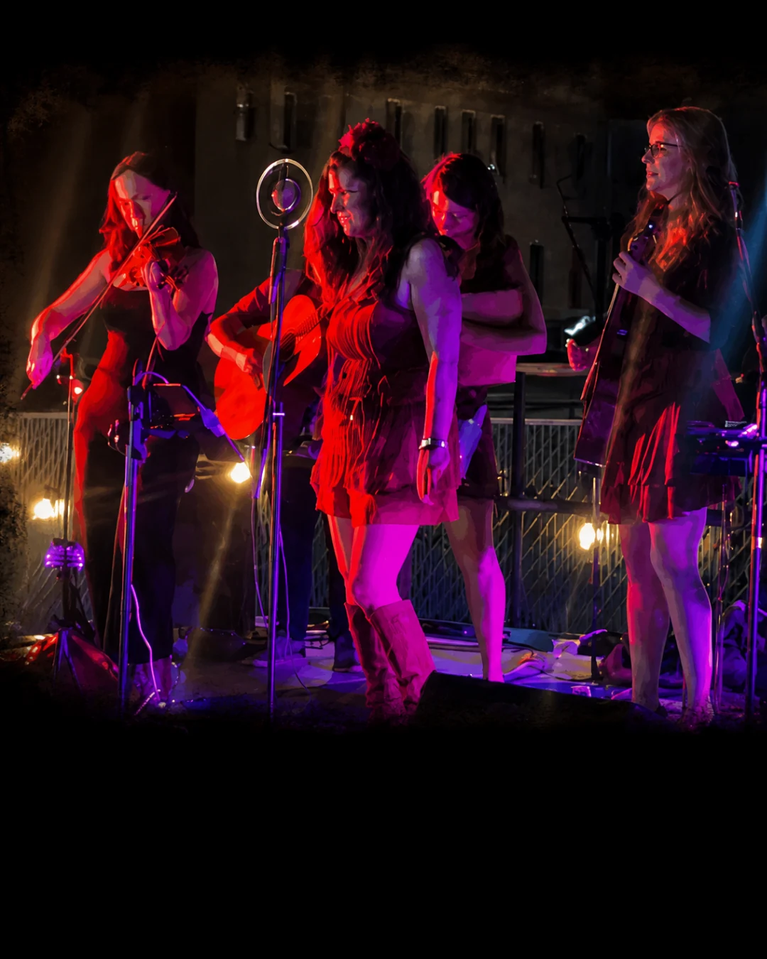 Jenny & The StreetWalkers gathered around a vintage microphone under red and purple stage lights